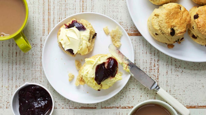 A stylised photograph looking down on table with a cream tea for two, with scones and jam and mugs of tea.